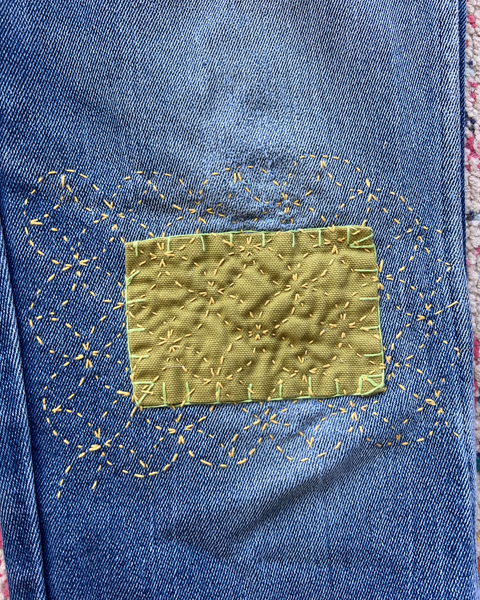 Close-up of a blue denim fabric with a yellow patch and decorative stitching.