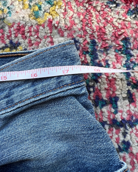 Measurements of a pair of blue jeans on a colorful patterned rug