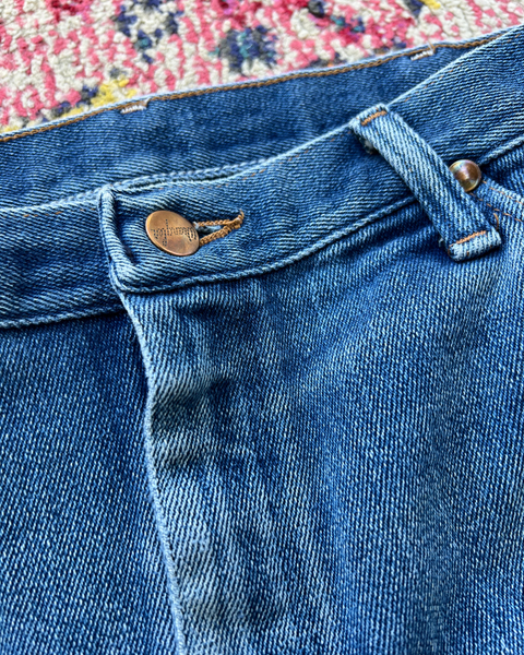 Close-up of blue denim jeans with a floral-patterned rug in the background