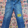 Blue jeans with a green patch on a colorful patterned rug