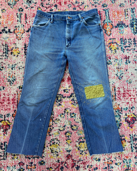 Blue jeans with a green patch on a colorful patterned rug