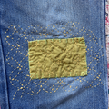 Close-up of a blue denim fabric with a yellow patch and decorative stitching.