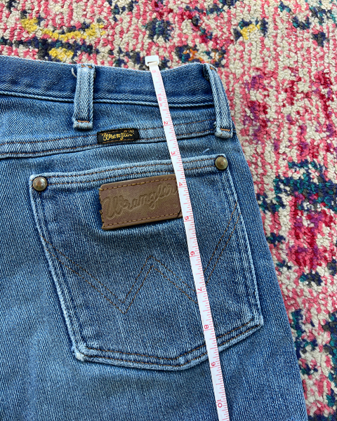 Blue jeans with a Wrangler label on a colorful patterned rug
