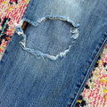 Close-up of a blue denim jeans with a heart-shaped hole on a colorful rug.