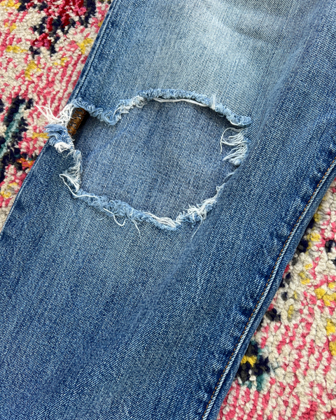 Close-up of a blue denim jeans with a heart-shaped hole on a colorful rug.