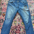 Distressed blue jeans with eye design on a colorful patterned rug