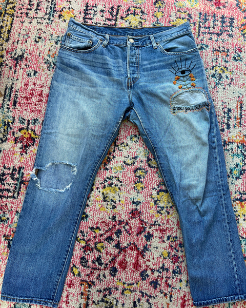Distressed blue jeans with eye design on a colorful patterned rug
