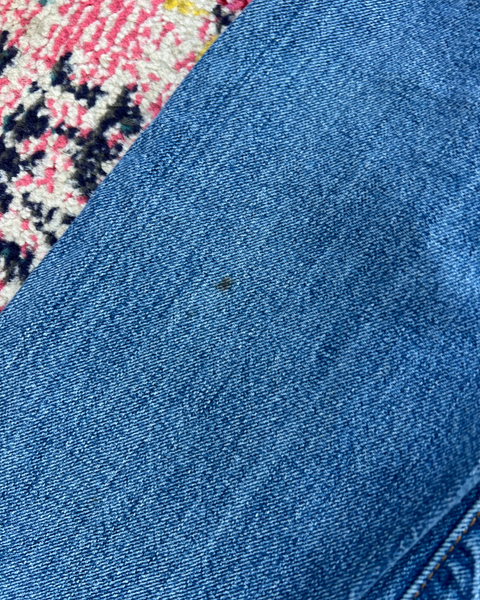 Close-up of blue denim fabric with a small black spot on a patterned rug background
