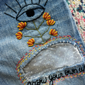 Embroidered design on denim fabric with flowers and an eye symbol.