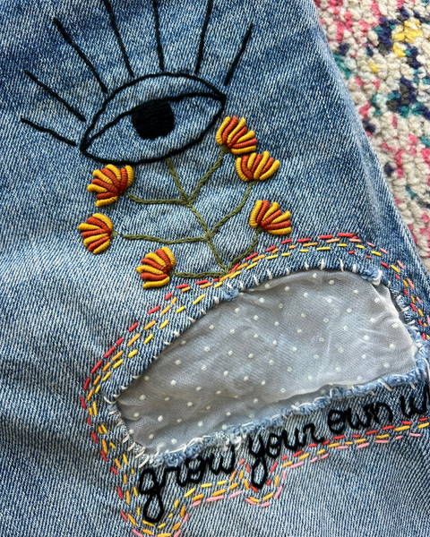 Embroidered design on denim fabric with flowers and an eye symbol.