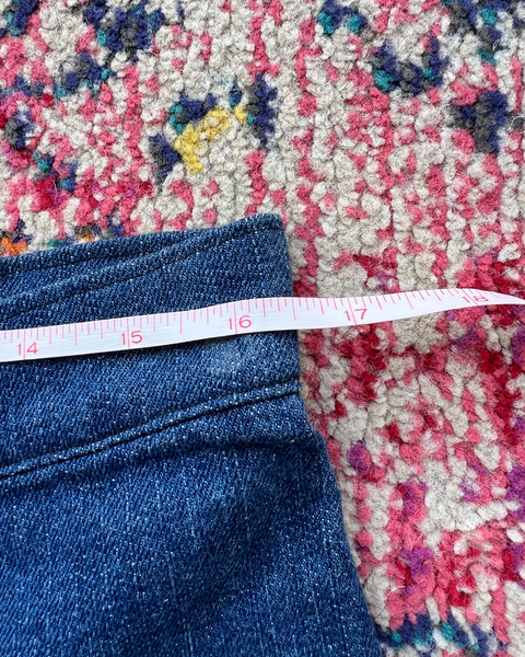 Close-up of a measuring tape on blue jeans with a colorful patterned rug underneath