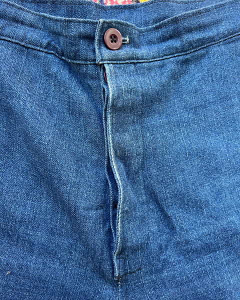 Close-up of blue denim fabric with a button and stitching detail.
