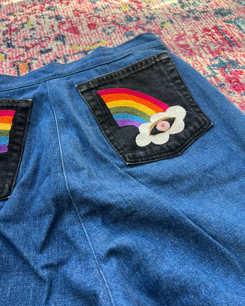 Blue denim jacket with a rainbow and cloud patch on a colorful fabric background