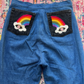 Blue jeans with rainbow and cloud patches on a colorful patterned surface