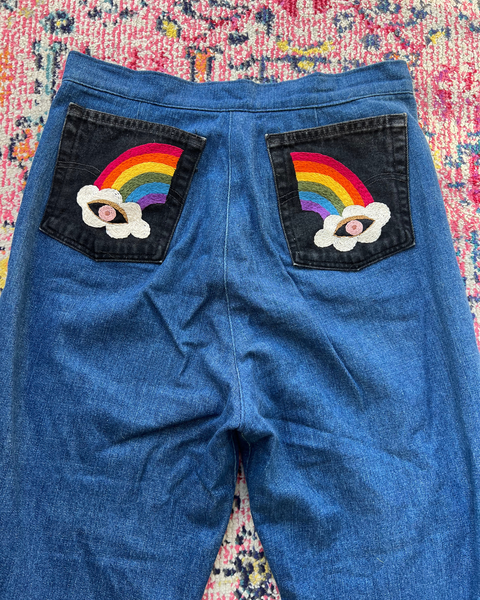 Blue jeans with rainbow and cloud patches on a colorful patterned surface