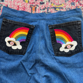 Blue denim shorts with rainbow and cloud patches on a colorful fabric background