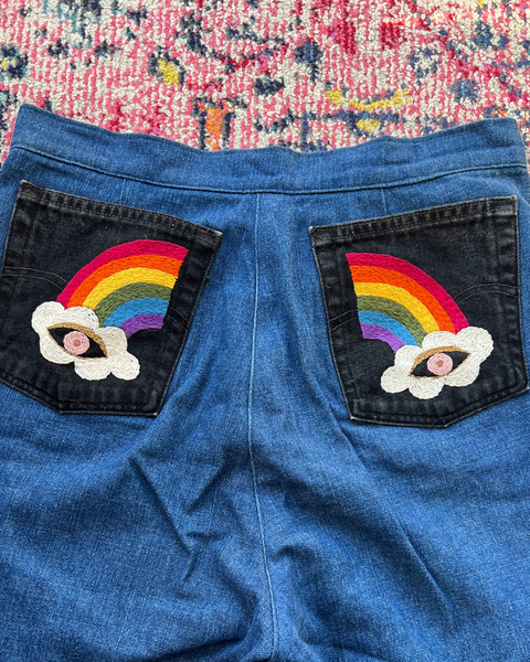 Blue denim shorts with rainbow and cloud patches on a colorful fabric background