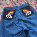 Blue denim shorts with rainbow and cloud patches on a colorful rug.