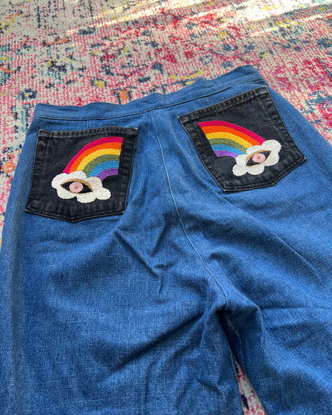 Blue denim shorts with rainbow and cloud patches on a colorful rug.