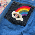 Embroidered rainbow and cloud patch on blue denim fabric.