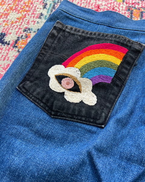 Embroidered rainbow and cloud patch on blue denim fabric.
