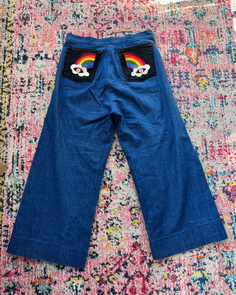 Blue pants with rainbow and cloud designs on a colorful patterned rug