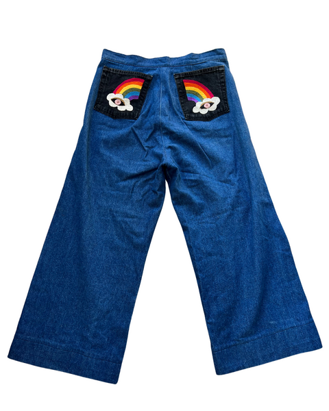 Blue pants with rainbow and cloud designs on the back pockets against a white background