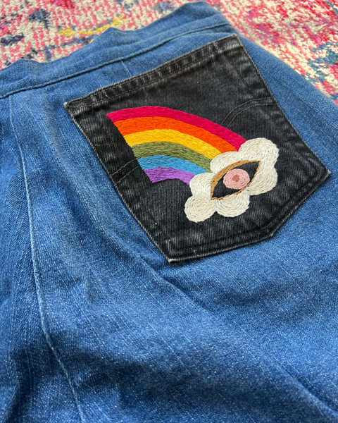 Blue denim fabric with a rainbow and cloud patch on a colorful background