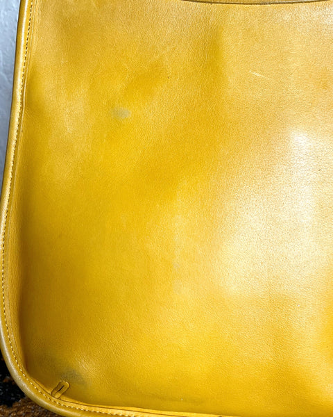 Close-up of a yellow leather bag with visible wear and tear.
