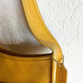 Close-up of a yellow Coach handbag with a textured white background