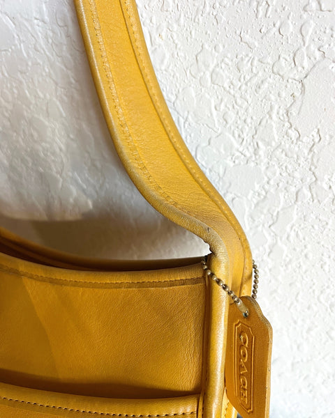 Close-up of a yellow Coach handbag with a textured white background