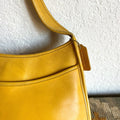 Yellow handbag with a visible brand logo against a textured white wall.