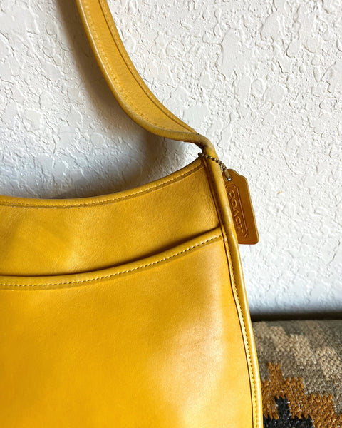 Yellow handbag with a visible brand logo against a textured white wall.